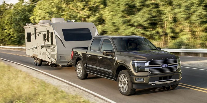 Brown Ford F-150 Platinum pickup truck towing a white and gray travel trailer on a highway.