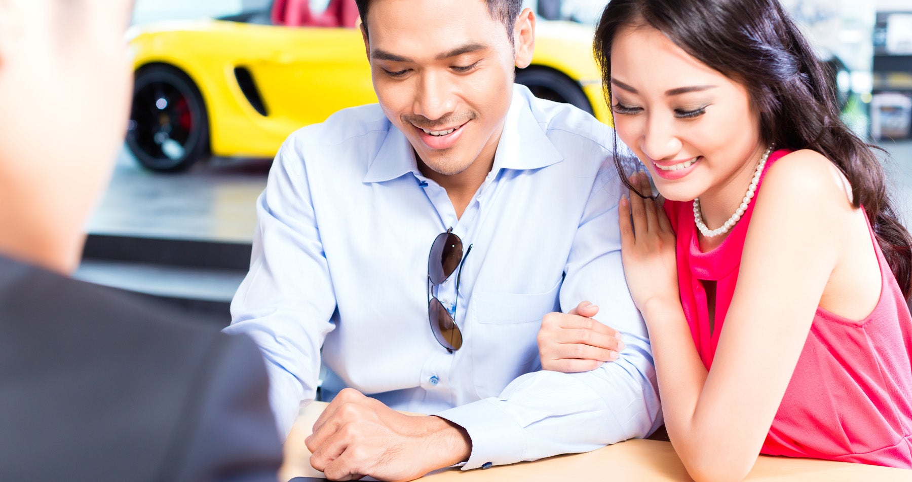 Smiling young couple looking down at paperwork with a car salesman