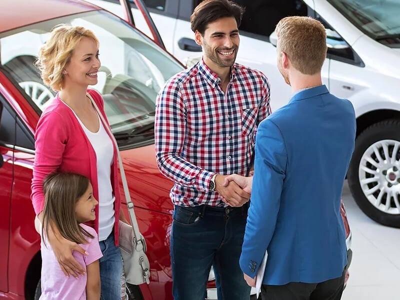 Smiling family shaking hands with a salesman in a car showroom