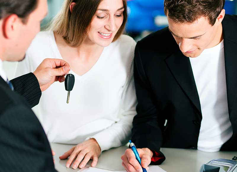 Young couple signing paperwork while salesman holds up new car keys