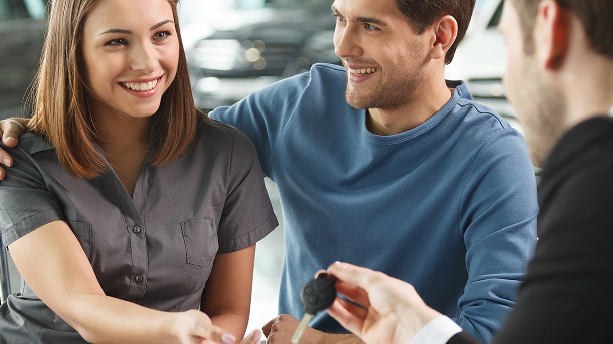 Smiling couple receiving new car keys from a dealership representative