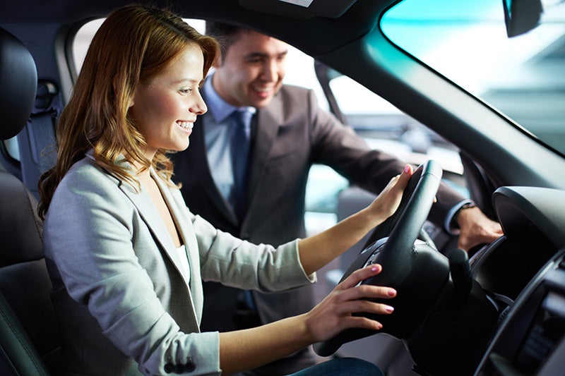 Smiling woman sitting in driver's seat with salesman looking on
