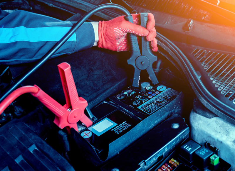 Close-up of a person using jumper cables on a car battery