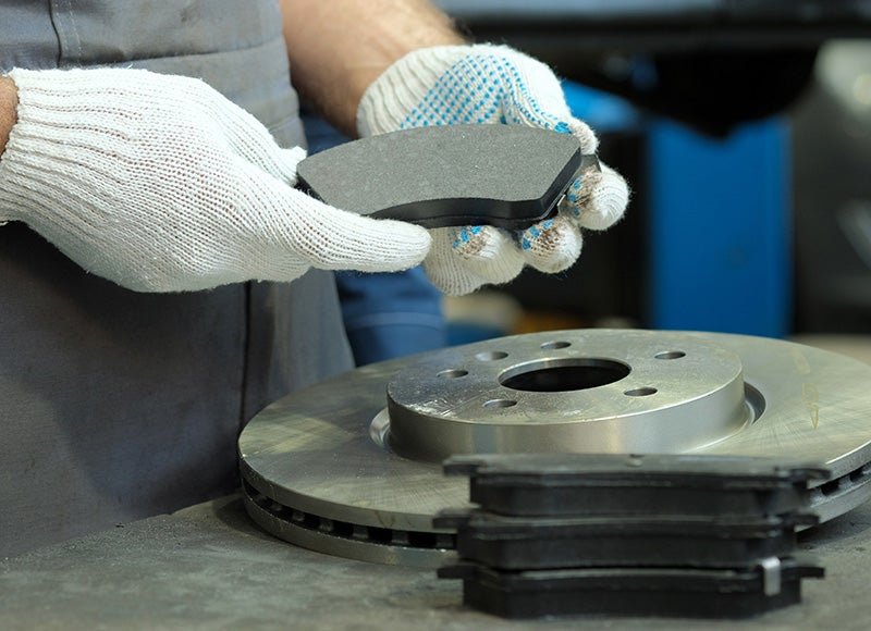 Mechanic holding a new brake pad over a car brake rotor